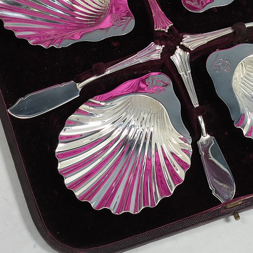 An Antique Victorian Sterling Silver set of four butter shells, having traditional scallop shapes, and sitting on three cast shell feet, together with four original butter knives in the Albany pattern, and all sitting in an original purple satin and velvet-lined presentation box. All made by Frances Higgins of London in 1884. The dimensions of this fine hand-made set of antique silver butter shells are length 12 cms (4.75 inches), width 10 cms (4 inches), with a total weight of approx. 385g (12.4 troy ounces).   