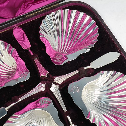 An Antique Victorian Sterling Silver set of four butter shells, having traditional scallop shapes, and sitting on three cast shell feet, together with four original butter knives in the Albany pattern, and all sitting in an original purple satin and velvet-lined presentation box. All made by Frances Higgins of London in 1884. The dimensions of this fine hand-made set of antique silver butter shells are length 12 cms (4.75 inches), width 10 cms (4 inches), with a total weight of approx. 385g (12.4 troy ounces).   