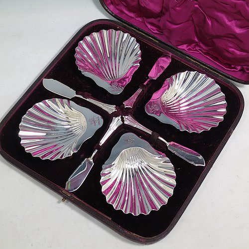 An Antique Victorian Sterling Silver set of four butter shells, having traditional scallop shapes, and sitting on three cast shell feet, together with four original butter knives in the Albany pattern, and all sitting in an original purple satin and velvet-lined presentation box. All made by Frances Higgins of London in 1884. The dimensions of this fine hand-made set of antique silver butter shells are length 12 cms (4.75 inches), width 10 cms (4 inches), with a total weight of approx. 385g (12.4 troy ounces).   