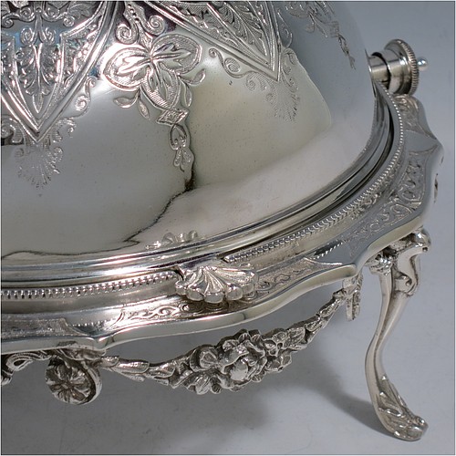 An Antique Victorian Silver Plated revolving top butter dish, having a hand-chased oval body with floral decoration and bead-edged border, a frosted glass removable internal liner, and sitting inside a cast frame with floral swags and four cast feet. All made in ca. 1880. The dimensions of this fine hand-made antique silver-plated butter dish are length 20 cms (8 inches), height 13 cms (5 inches), and width 15 cms (6 inches).    