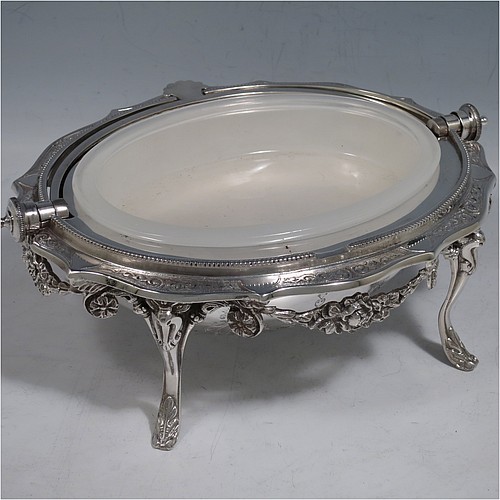 An Antique Victorian Silver Plated revolving top butter dish, having a hand-chased oval body with floral decoration and bead-edged border, a frosted glass removable internal liner, and sitting inside a cast frame with floral swags and four cast feet. All made in ca. 1880. The dimensions of this fine hand-made antique silver-plated butter dish are length 20 cms (8 inches), height 13 cms (5 inches), and width 15 cms (6 inches).    