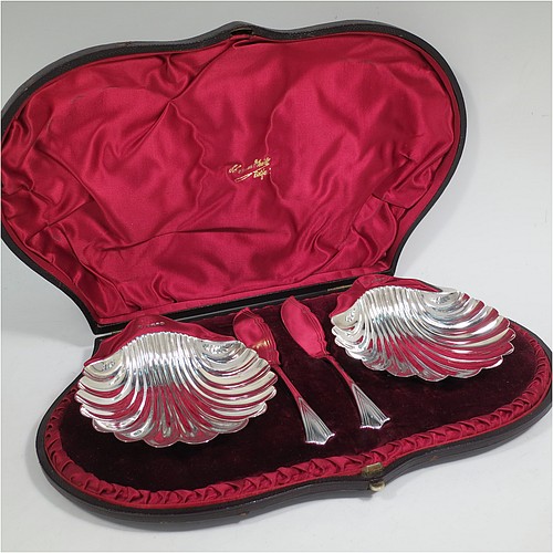 An Antique Victorian Sterling Silver pair of butter shells, having traditional scallop shapes, and sitting on three cast shell feet, together with a pair of original butter knives in the Albany pattern, and all sitting in an original maroon satin and velvet-lined presentation box. All made by John and William Deakin of Sheffield in 1886. The dimensions of this fine hand-made set of antique silver butter shells and knives are length 12.5 cms (5 inches), width 10.5 cms (4.25 inches), with a total weight of approx. 182g (5.9 troy ounces). 