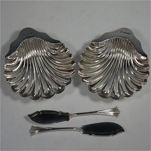 An Antique Victorian Sterling Silver pair of butter shells, having traditional scallop shapes, and sitting on three cast shell feet, together with a pair of original butter knives in the Albany pattern, and all sitting in an original maroon satin and velvet-lined presentation box. All made by John and William Deakin of Sheffield in 1886. The dimensions of this fine hand-made set of antique silver butter shells and knives are length 12.5 cms (5 inches), width 10.5 cms (4.25 inches), with a total weight of approx. 182g (5.9 troy ounces). 