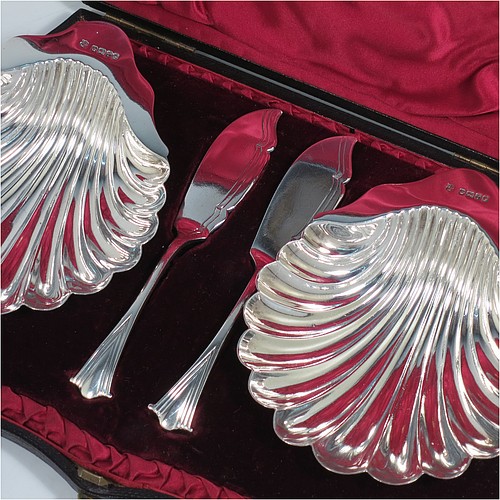 An Antique Victorian Sterling Silver pair of butter shells, having traditional scallop shapes, and sitting on three cast shell feet, together with a pair of original butter knives in the Albany pattern, and all sitting in an original maroon satin and velvet-lined presentation box. All made by John and William Deakin of Sheffield in 1886. The dimensions of this fine hand-made set of antique silver butter shells and knives are length 12.5 cms (5 inches), width 10.5 cms (4.25 inches), with a total weight of approx. 182g (5.9 troy ounces). 