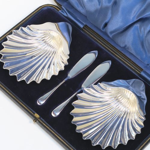 A handsome Antique Sterling Silver pair of butter shells, having traditional scallop shapes, and sitting on three ball feet, together with a pair of original butter knives, and all sitting in their original blue satin and velvet-lined presentation box. All made by Roberts and Belk of London in 1914. The dimensions of this fine hand-made set of antique silver butter shells and knives are length 12.5 cms (5 inches), width 10 cms (4 inches), with a total weight of approx. 148g (4.8 troy ounces).   