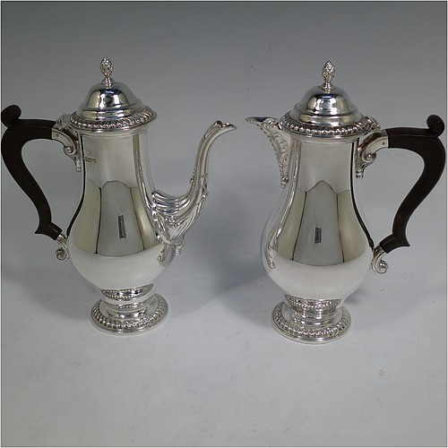 A very handsome pair of Sterling Silver cafe-au-lait pots in a Georgian style, having plain round bellied bodies with applied gadroon borders, with brown wooden scroll handles, hinged domed lids with cast pineapple finials, and sitting on pedestal feet. Made by the Barker Brothers of Birmingham in 1968/69. The dimensions of this fine hand-made pair silver cafe-au-lait pots are height 23 cms (9 inches), length of coffee pot 18.5 cms (7.25 inches), and they weigh a total of approx. 960g (31 troy ounces).   