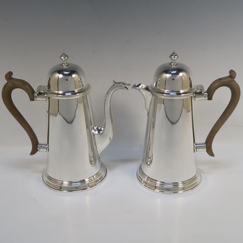 A very handsome Sterling Silver pair of cafe-au-lait pots, in a George I style, having very plain round bodies with tapering sides, light brown wooden scroll handles, domed hinged lids with finials, and sitting on collet feet. These handsome silver cafe-au-lait pots were made by F. and H. Ltd., of London in 1962. The dimensions of this fine pair of hand-made silver cafe-au-lait pots are height 21 cms (8.25 inches), length of coffee pot 20 cms (8 inches), and they weigh approx 1,062g (34.3 troy ounces).   