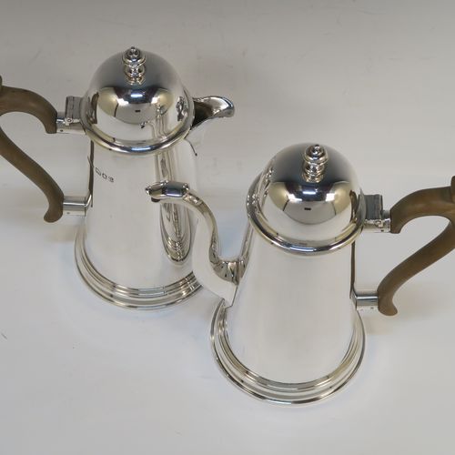 A very handsome Sterling Silver pair of cafe-au-lait pots, in a George I style, having very plain round bodies with tapering sides, light brown wooden scroll handles, domed hinged lids with finials, and sitting on collet feet. These handsome silver cafe-au-lait pots were made by F. and H. Ltd., of London in 1962. The dimensions of this fine pair of hand-made silver cafe-au-lait pots are height 21 cms (8.25 inches), length of coffee pot 20 cms (8 inches), and they weigh approx 1,062g (34.3 troy ounces).   