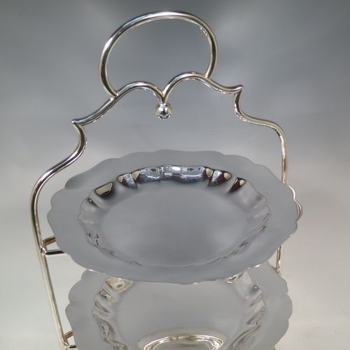 A pretty Antique Edwardian silver plated three-tier cake stand, having a suite of three plain removable plates with wavey-edged borders, sitting within a very pretty wire-work frame with scroll-work handle and four cast bun feet. Made in Sheffield in ca. 1910. The dimensions of this fine hand-made antique silver-plated cake stand are height 43 cms (17 inches), width at base 23 cms (9 inches), and diameter of plates 20 cms (8 inches).    