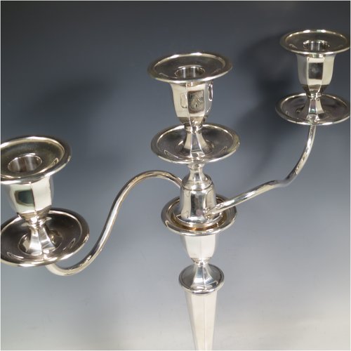 An Antique Edwardian Sterling Silver pair of candelabra in a round plain panelled style, having removable arms with three lights, panelled columns with round bases, double swirl panelled arms, capitals with removable nozzles and drip pans, and reed-edged borders. Made by Goldsmiths & Silversmiths of London in 1905. The dimensions of this fine hand-made pair of silver candelabra are height 44.5 cms (17.5 inches), and spread across arms 39.5 cms (15.5 inches).   