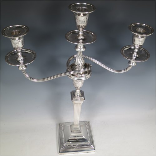 An Antique Edwardian Sterling Silver pair of candelabra in a Neoclassical style, having removable arms with three lights, fluted columns with stepped square bases, double swirl reeded arms, capitals with swags of flowers, removable nozzles with drip pans, and reed-edged borders. Made by George Hancock of London in 1903. The dimensions of this fine hand-made pair of silver candelabra are height 49 cms (19.25 inches), and spread across arms 37 cms (14.5 inches). Please note that these are crested on the bases.