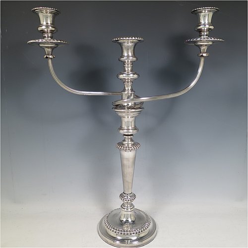 An Antique Georgian Old Sheffield Silver Plated pair of candelabra in a very elegant Regency style, having removable arms with three lights, with plain round baluster columns and bases, and plain reeded double swirl arms, removable nozzles with drip pans, and gadroon edged borders. Made in ca. 1815. The dimensions of this fine hand-made pair of Old Sheffield three-light candelabra are height 49 cms (19.25 inches), and spread across arms 39.5 cms (15.5 inches). Please note that the bases are crested.