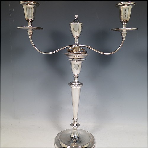 An Antique Georgian Old Sheffield Silver Plated pair of candelabra in a very elegant Neoclassical style, having removable arms with two lights and a central removable urn-shaped finial, with plain round baluster columns and bases, and plain double swirl arms, removable nozzles with drip pans, and reed-edged borders. Made in ca. 1790. The dimensions of this fine hand-made pair of Old Sheffield two-light candelabra are height 44 cms (17.3 inches), and spread across arms 36 cms (14 inches).    