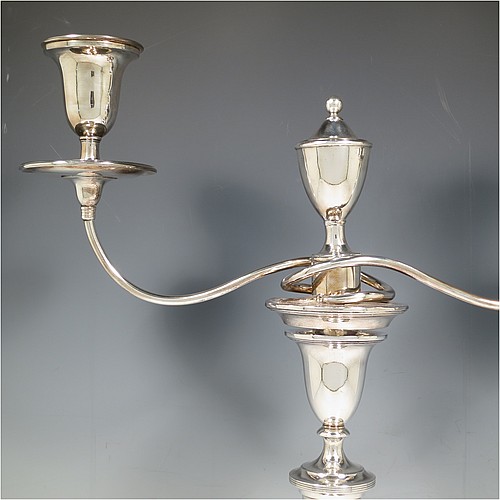 An Antique Georgian Old Sheffield Silver Plated pair of candelabra in a very elegant Neoclassical style, having removable arms with two lights and a central removable urn-shaped finial, with plain round baluster columns and bases, and plain double swirl arms, removable nozzles with drip pans, and reed-edged borders. Made in ca. 1790. The dimensions of this fine hand-made pair of Old Sheffield two-light candelabra are height 44 cms (17.3 inches), and spread across arms 36 cms (14 inches).    