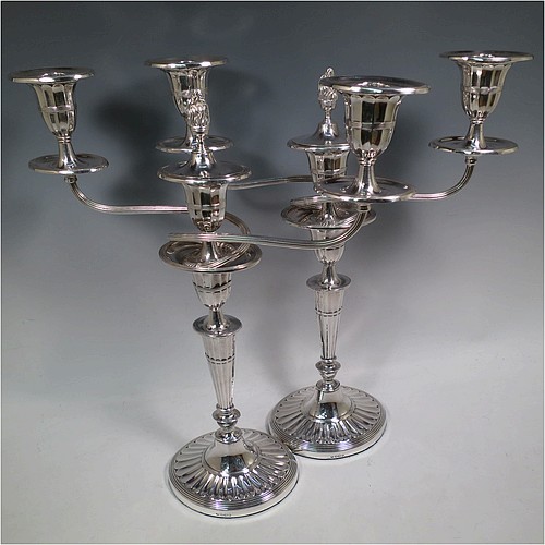 A very pretty pair of Antique Sterling Silver candelabra in a Neoclassical style, having removable arms with three lights, fluted columns with oval bases, double swirl and reeded arms, capitals with fluted and reeded decoration, removable nozzles with drip pans and a central flame extinguisher, and reed-edged borders. Made by William Hutton and Sons of Sheffield in 1913. The dimensions of this fine hand-made pair of antique silver candelabra are height 43 cms (17 inches), and spread across arms 34 cms (13.3 inches).    