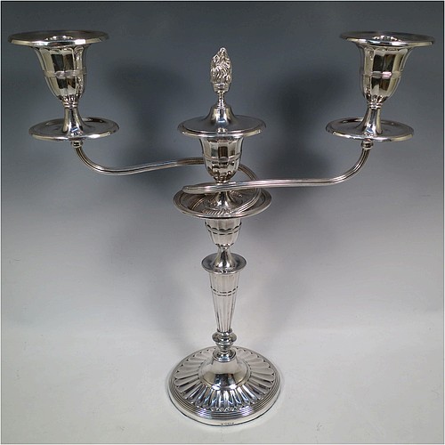 A very pretty pair of Antique Sterling Silver candelabra in a Neoclassical style, having removable arms with three lights, fluted columns with oval bases, double swirl and reeded arms, capitals with fluted and reeded decoration, removable nozzles with drip pans and a central flame extinguisher, and reed-edged borders. Made by William Hutton and Sons of Sheffield in 1913. The dimensions of this fine hand-made pair of antique silver candelabra are height 43 cms (17 inches), and spread across arms 34 cms (13.3 inches).    