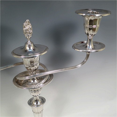 A very pretty pair of Antique Sterling Silver candelabra in a Neoclassical style, having removable arms with three lights, fluted columns with oval bases, double swirl and reeded arms, capitals with fluted and reeded decoration, removable nozzles with drip pans and a central flame extinguisher, and reed-edged borders. Made by William Hutton and Sons of Sheffield in 1913. The dimensions of this fine hand-made pair of antique silver candelabra are height 43 cms (17 inches), and spread across arms 34 cms (13.3 inches).    