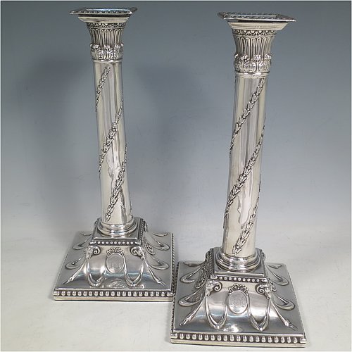 An Antique Georgian Sterling Silver pair of table candlesticks, in a Neoclassical style having square bases with hand-chased floral swags and rams heads, the columns with swirled garlands of flowers, scroll capitals with anthemion leaves, and removable nozzles with bead borders. Made by John Hoyland & Co., of Sheffield in 1777. The dimensions of theses fine antique silver candlesticks are height 28.5 cms (11.25 inches), bases 12.5 cms (5 inches) square.   