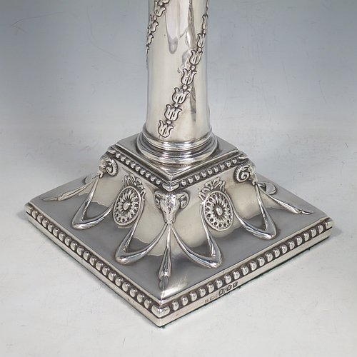 An Antique Georgian Sterling Silver pair of table candlesticks, in a Neoclassical style having square bases with hand-chased floral swags and rams heads, the columns with swirled garlands of flowers, scroll capitals with anthemion leaves, and removable nozzles with bead borders. Made by John Hoyland & Co., of Sheffield in 1777. The dimensions of theses fine antique silver candlesticks are height 28.5 cms (11.25 inches), bases 12.5 cms (5 inches) square.   