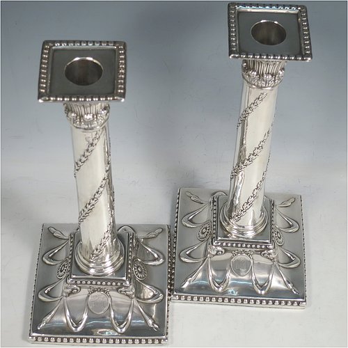 An Antique Georgian Sterling Silver pair of table candlesticks, in a Neoclassical style having square bases with hand-chased floral swags and rams heads, the columns with swirled garlands of flowers, scroll capitals with anthemion leaves, and removable nozzles with bead borders. Made by John Hoyland & Co., of Sheffield in 1777. The dimensions of theses fine antique silver candlesticks are height 28.5 cms (11.25 inches), bases 12.5 cms (5 inches) square.   