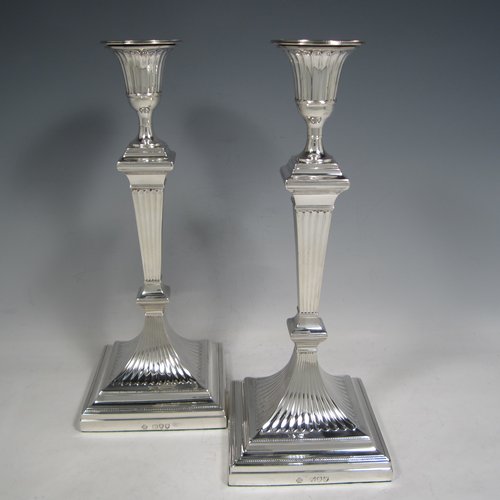 An Antique Victorian Sterling silver pair of large table candlesticks, in a Neoclassical style, having square cross-section bodies with hand-chased fluted decoration, tapering columns, and removable nozzles. Made by William Hutton of London in 1893. The dimensions of these fine hand-made silver candlesticks are height 30.5 cms (12 inches), and 12 cms (4.75 inches) square at bases.    