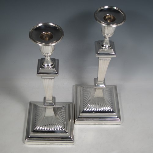 An Antique Victorian Sterling silver pair of large table candlesticks, in a Neoclassical style, having square cross-section bodies with hand-chased fluted decoration, tapering columns, and removable nozzles. Made by William Hutton of London in 1893. The dimensions of these fine hand-made silver candlesticks are height 30.5 cms (12 inches), and 12 cms (4.75 inches) square at bases.    