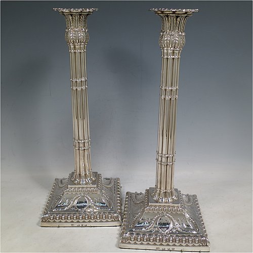 An Antique Georgian Sterling Silver pair of table candlesticks, in a Neoclassical style having square bases with bead borders, hand-chased floral swags and male head motifs, the columns in a bound palm-tree style with frond capitals, and removable nozzles. Made by John Cox of London in 1771. The dimensions of these fine antique silver candlesticks are height 32 cms (12.5 inches), bases 12.5 cms (5 inches) square. Please note that these candlesticks are crested.   