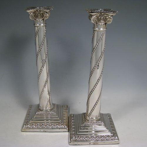 Antique Victorian sterling silver pair of table candlesticks, in a Neoclassical style having square stepped bases with hand-chased floral work, the columns with swirled garlands of flowers, scroll capitals with swags, and removable nozzles with gadroon borders. Made by William Hutton of London in 1901. Height 27.5 cms (10.75 inches), bases 11 cms (4.25 inches) square.