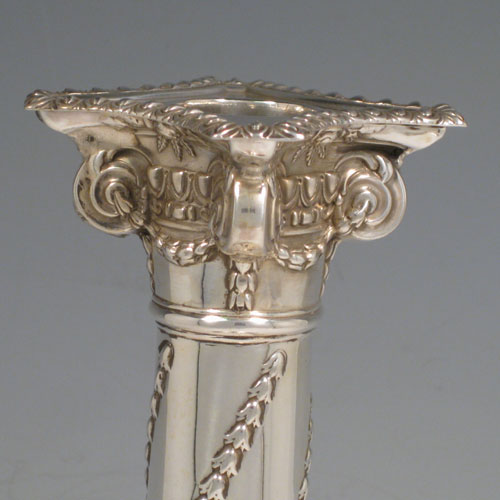 Antique Victorian sterling silver pair of table candlesticks, in a Neoclassical style having square stepped bases with hand-chased floral work, the columns with swirled garlands of flowers, scroll capitals with swags, and removable nozzles with gadroon borders. Made by William Hutton of London in 1901. Height 27.5 cms (10.75 inches), bases 11 cms (4.25 inches) square.