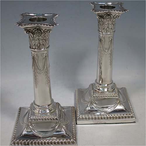 An Antique Edwardian Sterling Silver pair of candlesticks, in a Neoclassical Corinthian style with square bases and round straight-sided columns, having applied gadroon borders, hand-chased bows with swag decoration, and removable nozzles. Made by Henry Wilkinson of Sheffield in 1902. The dimensions of this fine pair of hand-made antique silver candlesticks are height 19 cms (7.5 inches), and the bases are 10 cms (4 inches) square.    