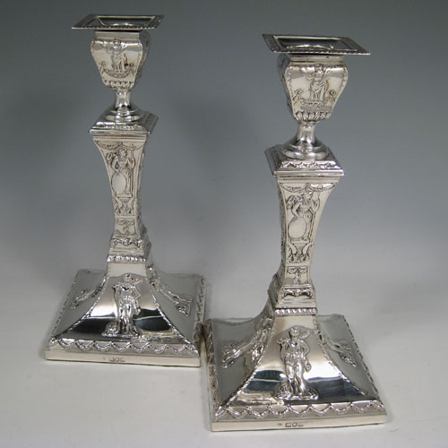 Antique Edwardian sterling silver pair of square-based candlesticks decorated in a neoclassical style with swags and greco-roman figures. Made by William Comyns of London in 1904. Height 24 cms (9.5 inches), width at base 11.5 cms (4.5 inches).