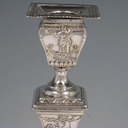 Antique Edwardian sterling silver pair of square-based candlesticks decorated in a neoclassical style with swags and greco-roman figures. Made by William Comyns of London in 1904. Height 24 cms (9.5 inches), width at base 11.5 cms (4.5 inches).