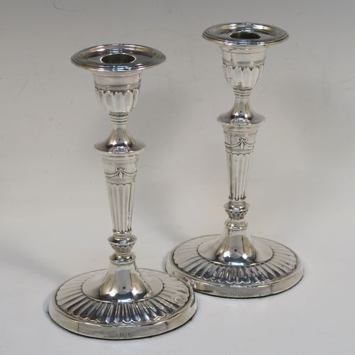 A very pretty pair of Antique Victorian Sterling Silver candlesticks, having Neoclassical style oval shaped bodies, with hand-chased fluted decoration, reeded borders, bows and swags, and removable nozzles. These beautiful antique silver candlesticks were made by Holland, Aldwinckle, and Slater of London in 1894. The dimensions of these fine hand-made pair of antique silver table candlesticks are height 18.5 cms (7.25 inches), length at base 10 cms (4 inches), and width at base 7.5 cms (3 inches).  