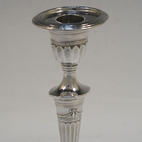 A very pretty pair of Antique Victorian Sterling Silver candlesticks, having Neoclassical style oval shaped bodies, with hand-chased fluted decoration, reeded borders, bows and swags, and removable nozzles. These beautiful antique silver candlesticks were made by Holland, Aldwinckle, and Slater of London in 1894. The dimensions of these fine hand-made pair of antique silver table candlesticks are height 18.5 cms (7.25 inches), length at base 10 cms (4 inches), and width at base 7.5 cms (3 inches).  