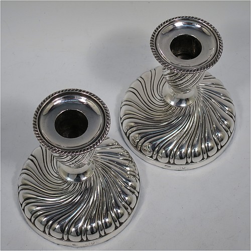 A very pretty Antique Victorian Sterling Silver pair of small candlesticks, having round bodies with hand-chased swirl-fluted decoration, and removable nozzles with applied gadroon borders. Made by Henry Holland of London in 1895. The dimensions of these fine hand-made antique silver candlesticks are height 10 cms (4 inches), and the bases are 9 cms (3.5 inches) in diameter.    