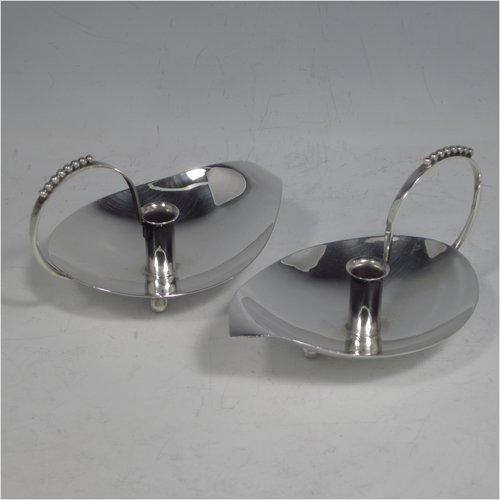 A Sterling Silver modernistic style pair of small chamber-sticks for taper candles, having plain leaf-form bodies, scroll handles with applied bead-work, and sitting on three ball feet. Made by A. E. Jones of Birmingham in 1960. The dimensions of these fine hand-made silver chambersticks are length 11 cms (4.25 inches), width 7 cms (2.75 inches), height 6 cms (2.3 inches), and they weigh a total of approx. 98g (3.2 troy ounces).