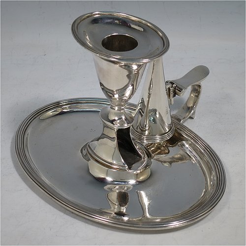 An Antique Georgian Sterling Silver chamber-stick, having an oval body, a plain scroll handle with thumb-piece, an original removable dunce-cap extinguisher, an original removable nozzle, and with applied reed-edged borders. Made by William Bennett of London in 1802. The dimensions of this fine hand-made antique silver chamberstick are width 16 cms (6.3 inches), depth 15 cms (6 inches), height 10 cms (4 inches), and it weighs approx. 319g (10.3 troy ounces).    