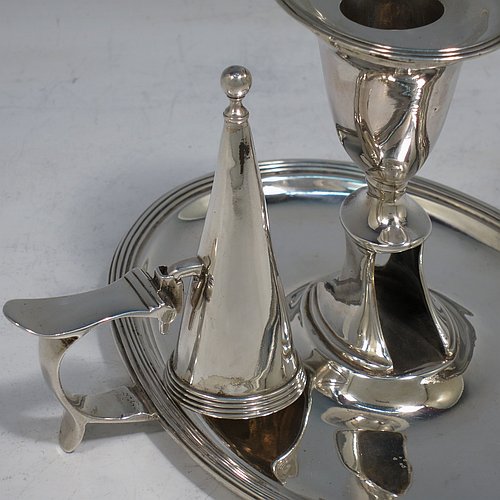 An Antique Georgian Sterling Silver chamber-stick, having an oval body, a plain scroll handle with thumb-piece, an original removable dunce-cap extinguisher, an original removable nozzle, and with applied reed-edged borders. Made by William Bennett of London in 1802. The dimensions of this fine hand-made antique silver chamberstick are width 16 cms (6.3 inches), depth 15 cms (6 inches), height 10 cms (4 inches), and it weighs approx. 319g (10.3 troy ounces).    