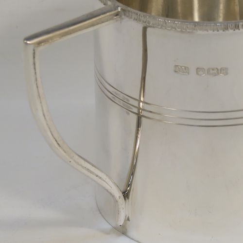 A very elegant Sterling Silver Georgian style christening mug, having a plain round body with a band of hand-chased reeded decoration, an applied egg and dart top border, a scroll handle with flat top, and sitting on a flat base. This handsome silver christening mug was made by Emile Viner of Sheffield in 1933. The dimensions of this fine hand-made silver christening mug are height 8 cms (3 inches), length 10 cms (4 inches), and it weighs approx. 137g (4.4 troy ounces).   