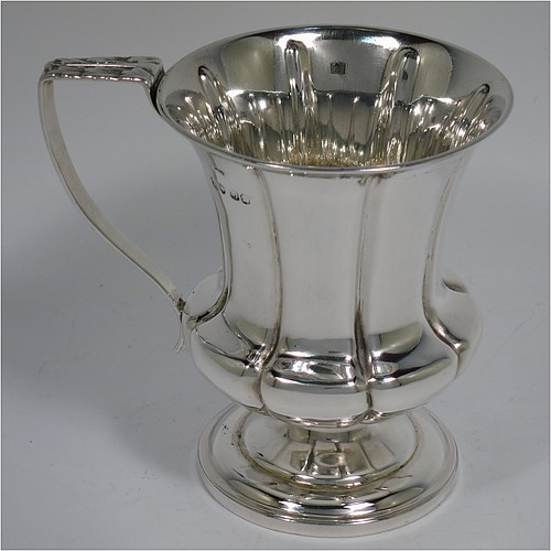 An Antique Georgian Sterling Silver christening mug, having a round bellied body, with hand-chased melon style fluted decoration, an acanthus leaf scroll handle, and sitting on a pedestal foot. Made by William Bateman of London in 1829. The dimensions of this fine hand-made antique silver christening mug are height 11 cms (4.3 inches), length 11.5 cms (4.5 inches), and it weighs approx. 185g (6 troy ounces).    