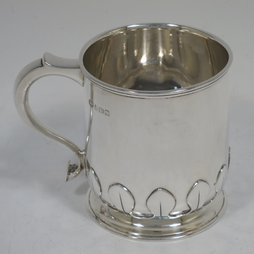 A handsome and unusual Sterling Silver christening mug, having a plain round body with tapering sides and tucked under belly with applied cut-card work, a scroll handle, and sitting on a pedestal foot. Made by Alexander Clarke of Birmingham in 1922. The dimensions of this fine hand-made silver christening mug are height 8 cms (3.25 inches), length 11 cms (4.25 inches), and it weighs approx. 200g (6.5 troy ounces).   