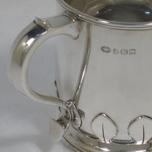 A handsome and unusual Sterling Silver christening mug, having a plain round body with tapering sides and tucked under belly with applied cut-card work, a scroll handle, and sitting on a pedestal foot. Made by Alexander Clarke of Birmingham in 1922. The dimensions of this fine hand-made silver christening mug are height 8 cms (3.25 inches), length 11 cms (4.25 inches), and it weighs approx. 200g (6.5 troy ounces).   