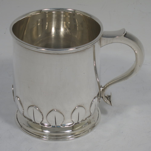 A handsome and unusual Sterling Silver christening mug, having a plain round body with tapering sides and tucked under belly with applied cut-card work, a scroll handle, and sitting on a pedestal foot. Made by Alexander Clarke of Birmingham in 1922. The dimensions of this fine hand-made silver christening mug are height 8 cms (3.25 inches), length 11 cms (4.25 inches), and it weighs approx. 200g (6.5 troy ounces).   