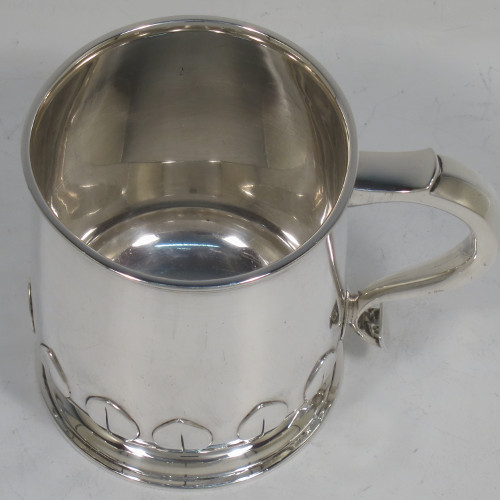 A handsome and unusual Sterling Silver christening mug, having a plain round body with tapering sides and tucked under belly with applied cut-card work, a scroll handle, and sitting on a pedestal foot. Made by Alexander Clarke of Birmingham in 1922. The dimensions of this fine hand-made silver christening mug are height 8 cms (3.25 inches), length 11 cms (4.25 inches), and it weighs approx. 200g (6.5 troy ounces).   