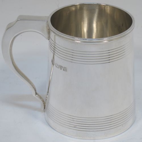 A very elegant Sterling Silver Georgian style christening mug, having a plain round body with two bands of hand-chased reeded decoration, a scroll handle with flat top, and sitting on a flat base. Made by Jays of Oxford Street, London in 1923. The dimensions of this fine hand-made silver christening mug are height 8 cms (3 inches), length 10 cms (4 inches), and it weighs approx. 160g (5.2 troy ounces).  