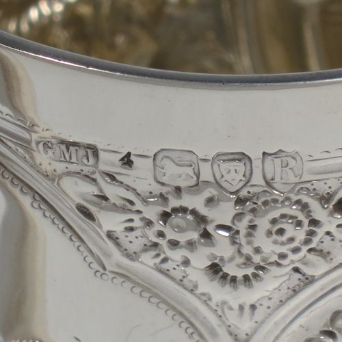 A very pretty Antique Victorian Sterling Silver christening mug, having a round straight-sided body with tucked under belly, all hand-chased with  floral and scroll-work decoration, a central vacant half-moon style cartouche, a plain loop handle, and all sitting on a collet foot. Made by George Maudsley Jackson of London in 1892. The dimensions of this fine hand-made antique silver christening mug are height 9.5 cms (3.75 inches), diameter at lip 7 cms (2.75 inches), and it weighs approx. 149g (4.8 troy ounces).   