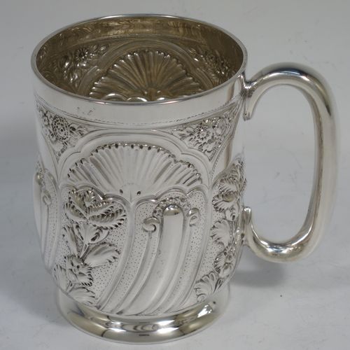 A very pretty Antique Victorian Sterling Silver christening mug, having a round straight-sided body with tucked under belly, all hand-chased with  floral and scroll-work decoration, a central vacant half-moon style cartouche, a plain loop handle, and all sitting on a collet foot. Made by George Maudsley Jackson of London in 1892. The dimensions of this fine hand-made antique silver christening mug are height 9.5 cms (3.75 inches), diameter at lip 7 cms (2.75 inches), and it weighs approx. 149g (4.8 troy ounces).   