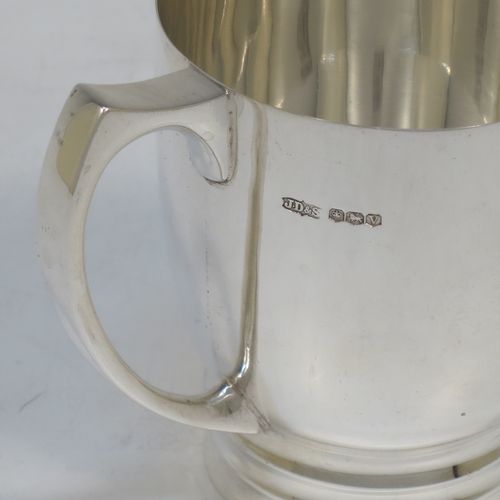 A very handsome Art Deco style Sterling Silver christening mug, having a plain round body with tapering sides, a scroll handle, and sitting on a pedestal foot with banded decoration. Made by James Dixon and Sons of Sheffield in 1938. The dimensions of this fine hand-made Art Deco silver christening mug are height 8 cms (3.25 inches), length 9 cms (3.5 inches), and it weighs approx. 165g (5.3 troy ounces).