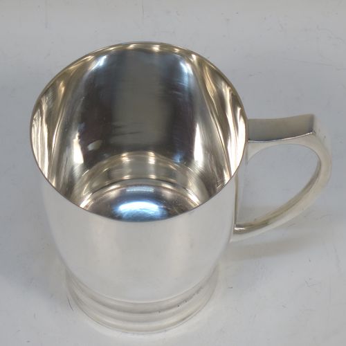 A very handsome Art Deco style Sterling Silver christening mug, having a plain round body with tapering sides, a scroll handle, and sitting on a pedestal foot with banded decoration. Made by James Dixon and Sons of Sheffield in 1938. The dimensions of this fine hand-made Art Deco silver christening mug are height 8 cms (3.25 inches), length 9 cms (3.5 inches), and it weighs approx. 165g (5.3 troy ounces).