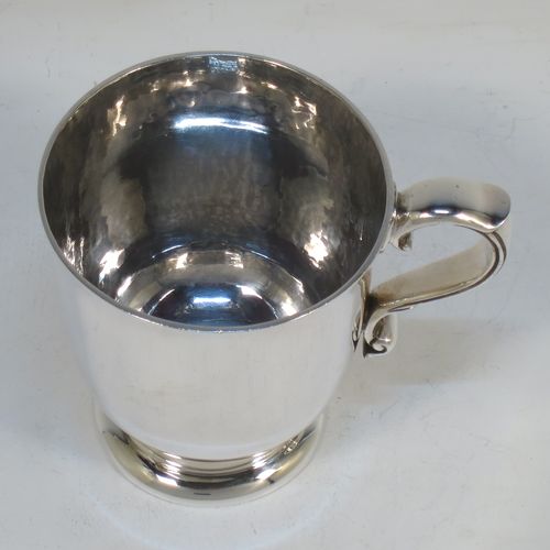 A handsome and heavy Antique Edwardian Sterling Silver christening mug, having a plain round straight-sided body with tucked under belly, a hand-hammered interior, a scroll handle with hand-chased reeded decoration, and sitting on a pedestal foot. Made by Jays of Chester in 1909. The dimensions of this fine hand-made antique silver christening mug are height 8 cms (3 inches), length 9.5 cms (3.75 inches), and it weighs approx. 161g (5.2 troy ounces).  